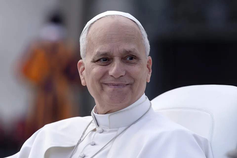 A dignified figure in formal attire smiles while seated outdoors, showcasing an expression of warmth and tranquility