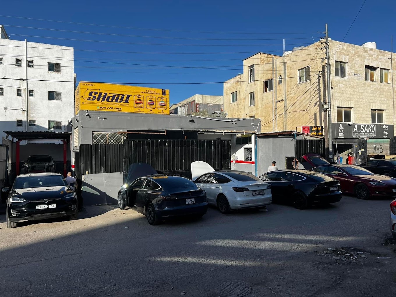 Tesla cars parked in front of a closed shop with a yellow container on its roof that reads "Shadi" 