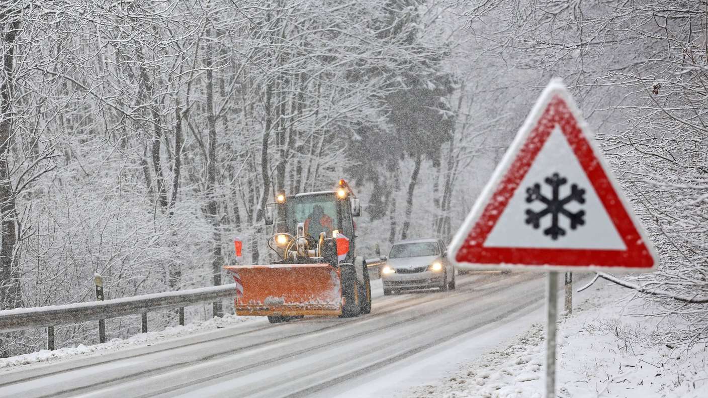 Schneebedeckte Straße mit Auto und Schneeschiebefahrzeug.