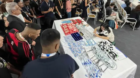 Tom Ingham/BBC A crowd stare at a table full of souvenirs at the Chinese pavilion at COP30 in Belém, Brazil