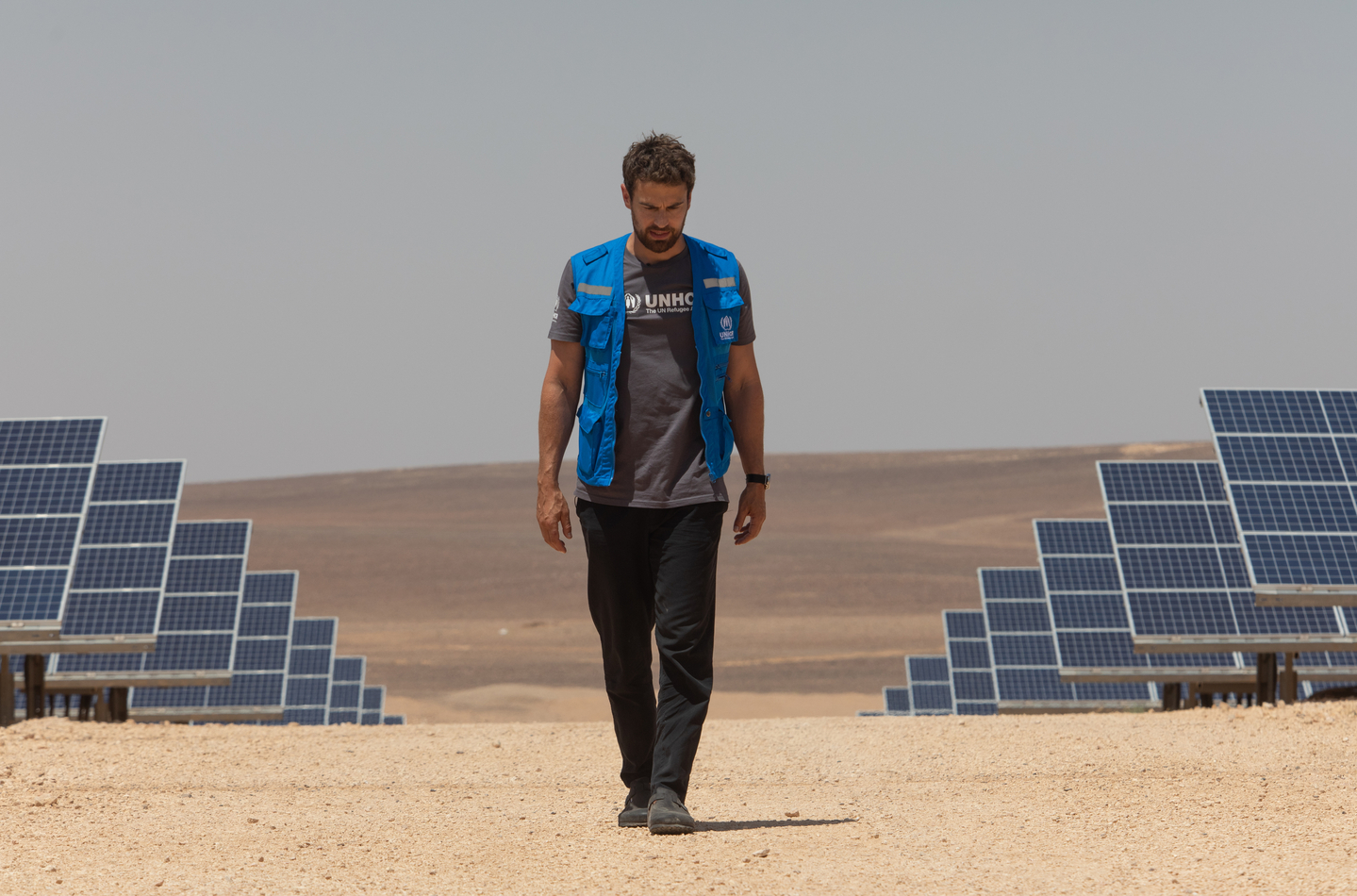 Actor Theo James walks amid solar panels powering the Azraq Refugee Camp in Jordan on July 25, 2023. The solar plant, which was funded by IKEA Foundation, provides the camp with 79 percent of its electricity needs. [UNITED NATIONS HIGH COMMISSIONER FOR REFUGEES]