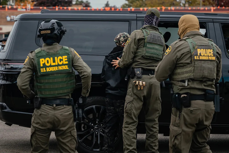U.S. Border Patrol agents detaining a person beside a black SUV in a public area