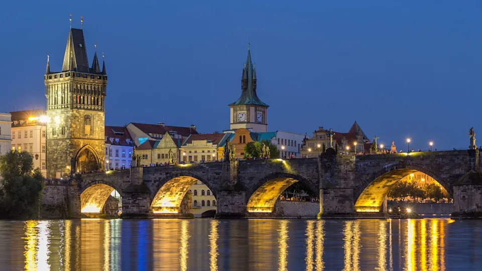 The Charles Bridge day to night transition timelapse over the Vltava River reflected in water in Prague, Czech Republic. Illuminater buildings and old town tower