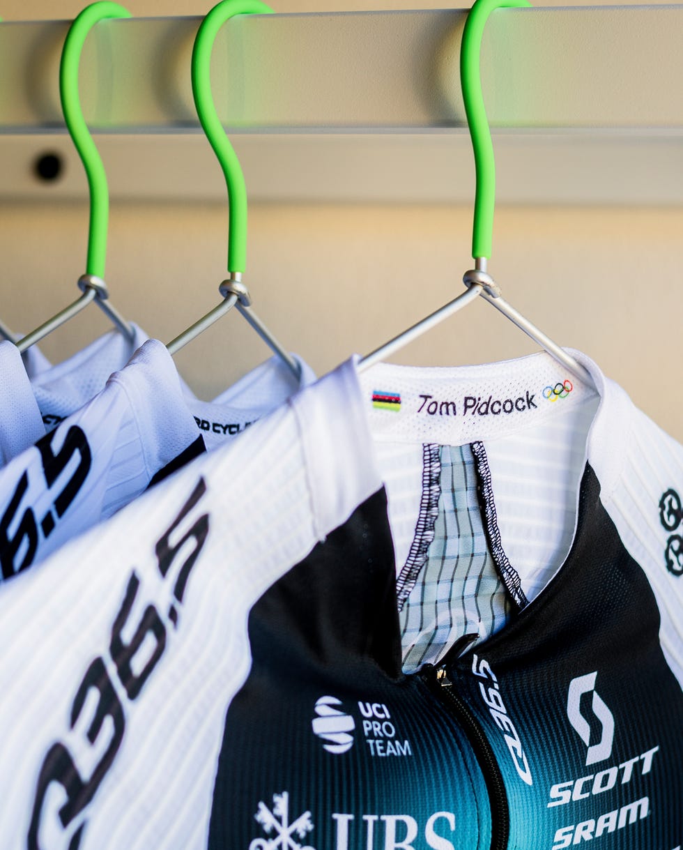 Cycling jerseys hanging on green hooks.