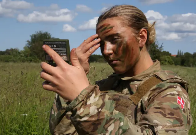 Female soldier for Danish Royal Life Guards apply camouflage paint to her face during training exercise for Hovelte, Denmark, June 11, 2025