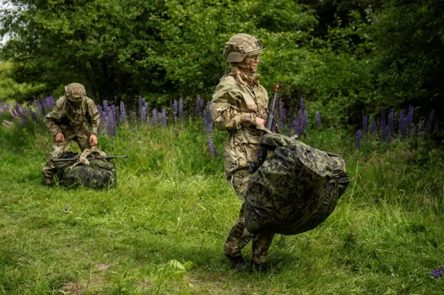 Female conscript for Danish army, wear military fatigues and helmet, carri rifle and large bag