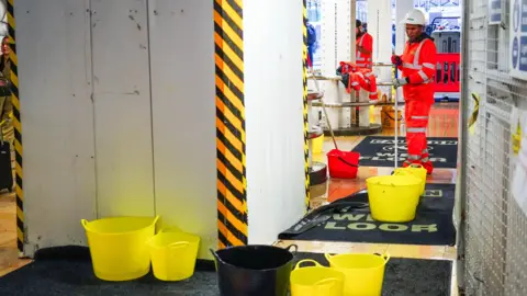 PA Media Several yellow and black plastic buckets collect rain water at Paddington Station in London as Storm Claudia hits the UK. 