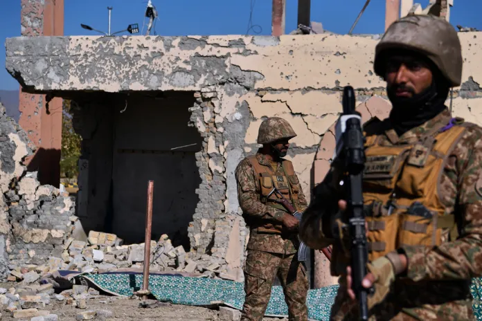 Army soldiers stand guard next to a damaged building.