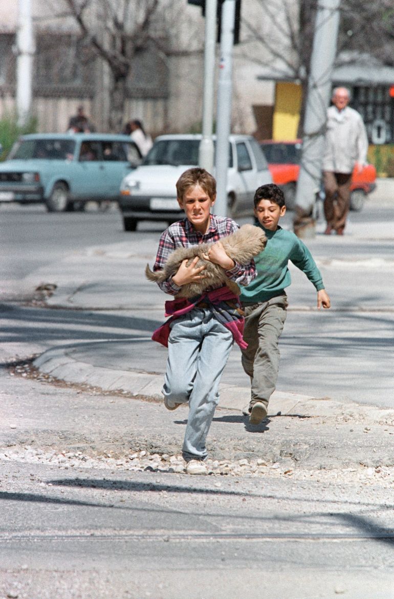 Carrying his dog, a boy springs across a central intersection which is sometimes targeted by snipers on Thursday