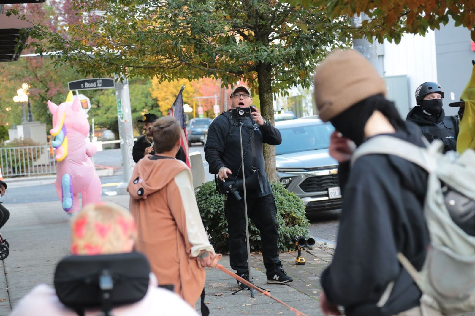 man next to phone camera on a tripod with several people around him on a sidewalk
