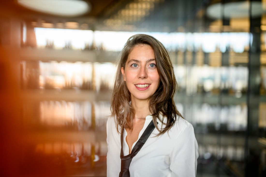 Cansu Canca has brown hair, blue eyes and a white collared shirt. She is smiling against a sleek backdrop.