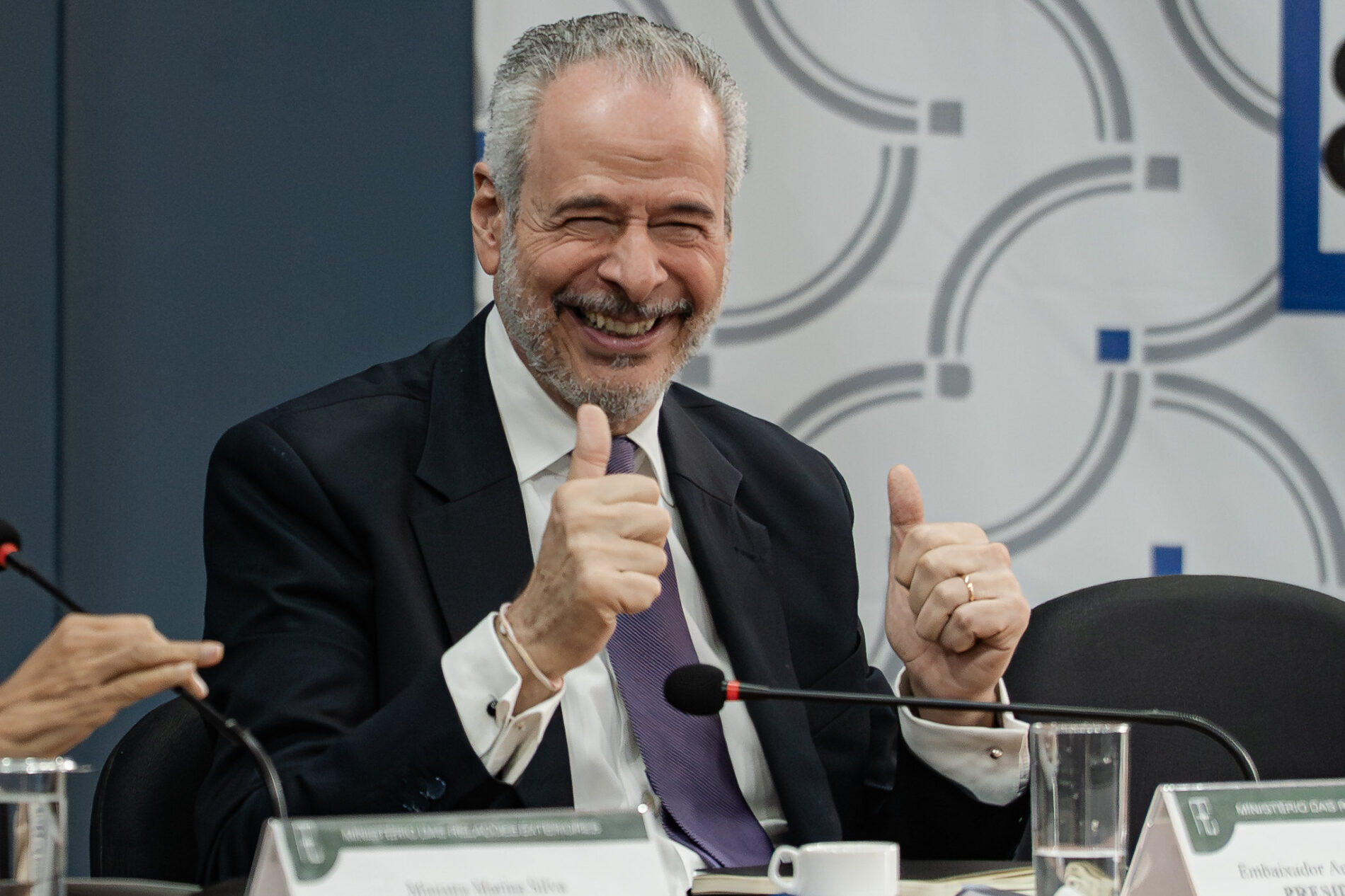 A man in a suit gives a "thumbs up" to the camera.