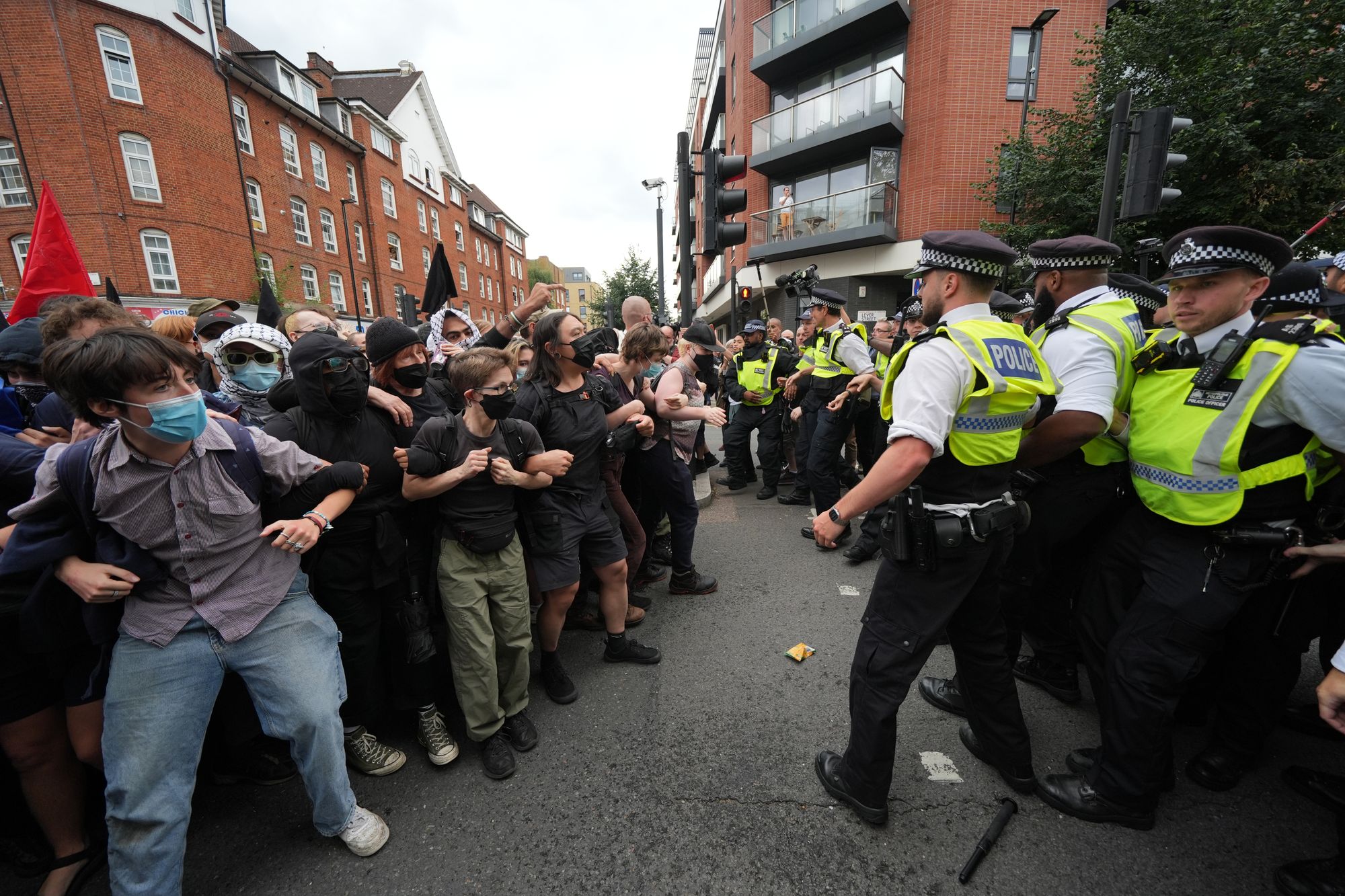 Police form a barrier in front of masked protesters outside the Thistle City Barbican Hotel in central London, which houses asylum seekers, in Summer 2025. The number of people housed in asylum hotels is on the rise.