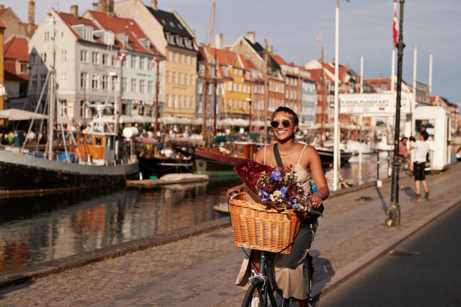 Happy young woman with sunglasses enjoying while riding bicycle on Nyhavn pier in city