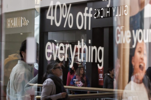 Black Friday shoppers are reflected in the window of a storefront touting a 40% off everything at Hillsdale Shopping Center Nov. 28 in San Mateo, Calif. (Dai Sugano/Bay Area News Group)