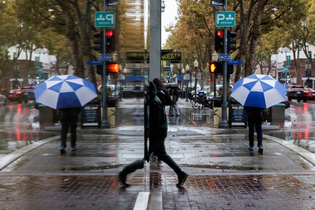 Pedestrians are reflected in shop windows as they walk in the rain in downtown Palo Alto as a storm arrives in the Bay Area on Oct. 13, 2025. (Dai Sugano/Bay Area News Group)