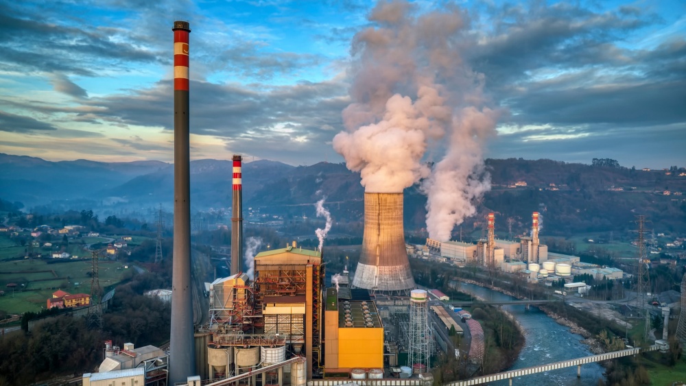 Smoke coming out of the chimneys of a power plant located next to a river.