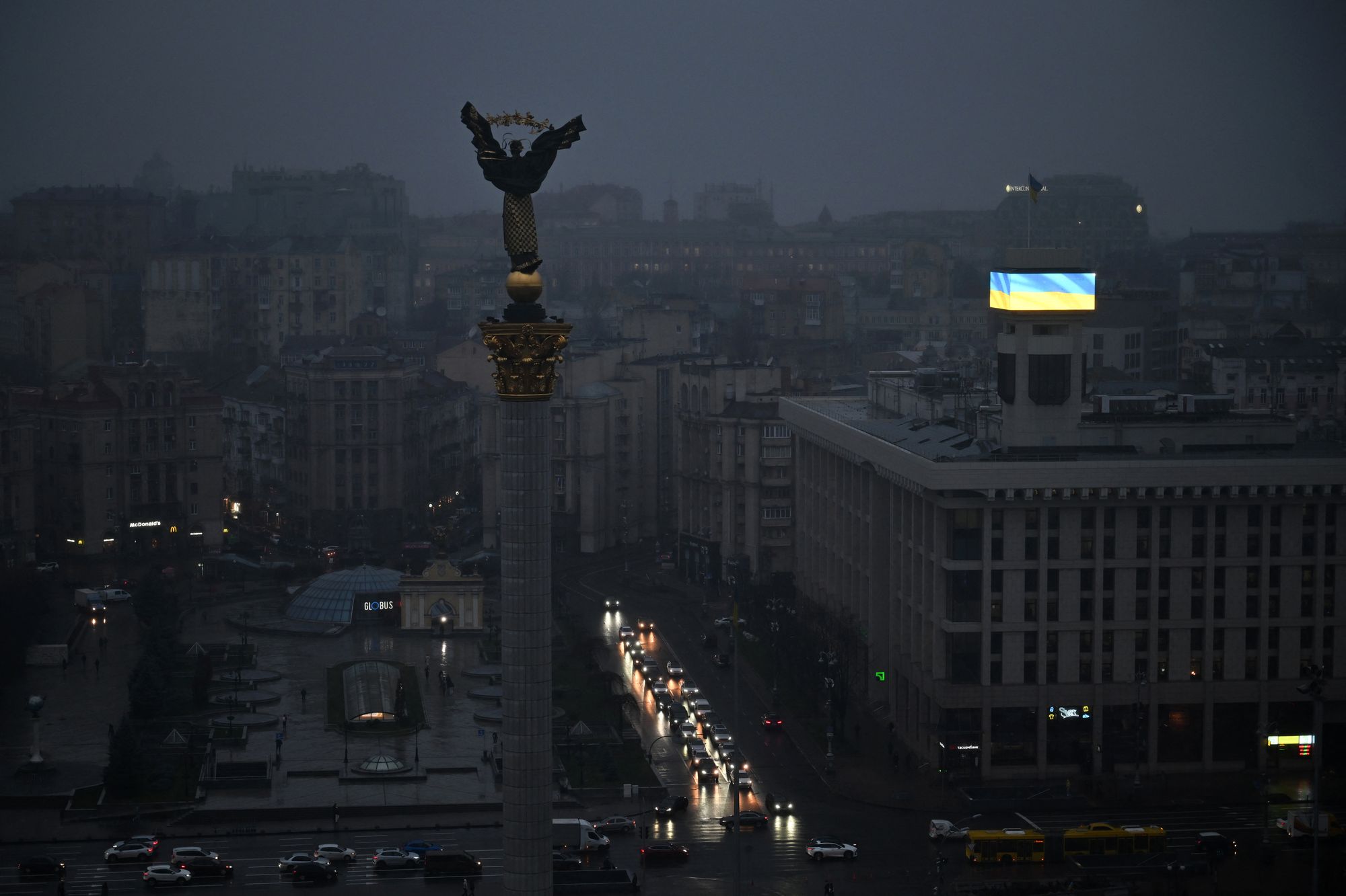 Cars drive along Independence Square as a Ukrainian flag is displayed on a big screen during a power outage in Kyiv