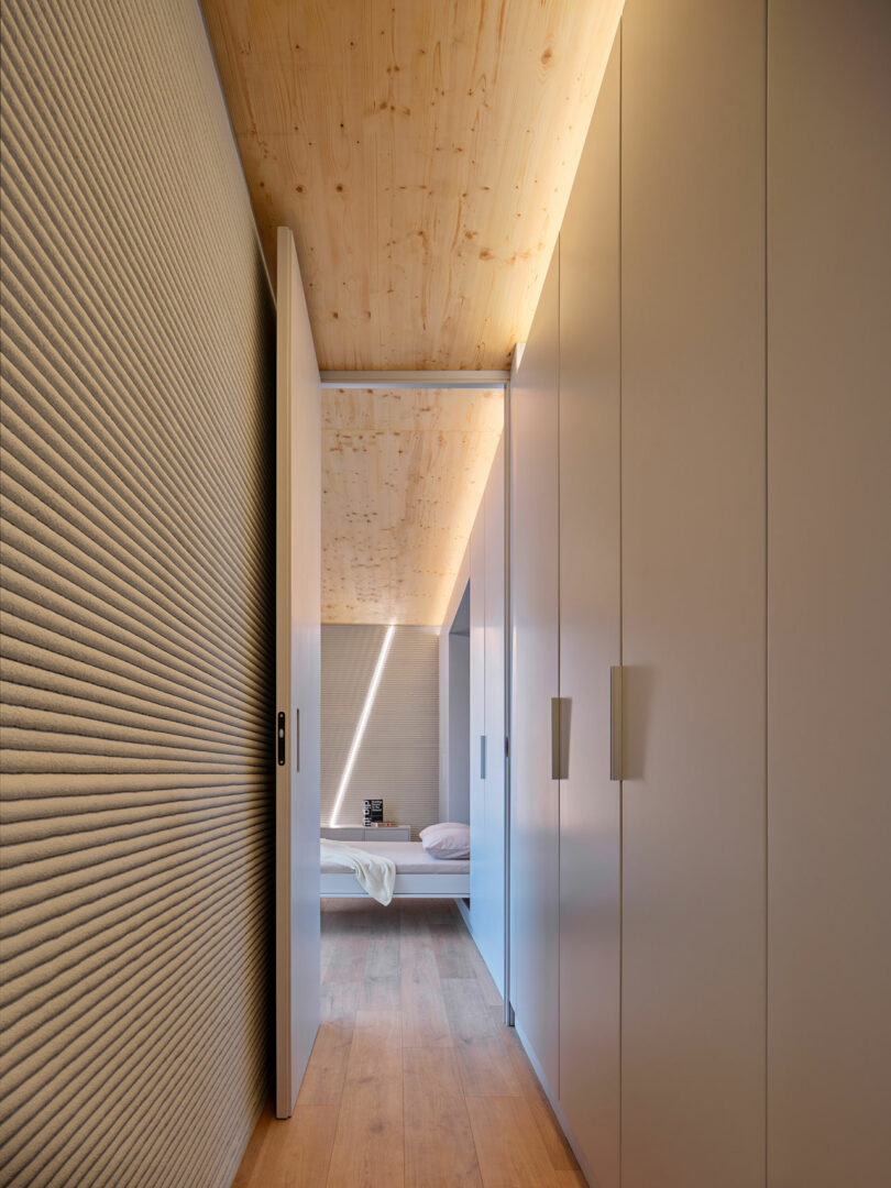 Minimalist hallway with textured wall, wooden ceiling, built-in closets, and a view into a modern bedroom with natural light.