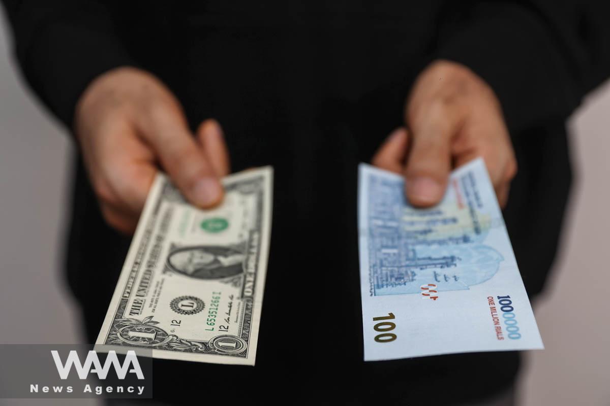 A currency dealer holds a U.S one-dollar bill and Iranian rial as the value of the Iranian Rial drops, in Tehran