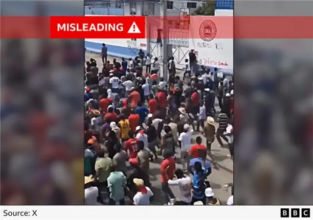 A screenshot from a video showing hundreds of people marching in a street, with sign for a Haitian government department visible in the background