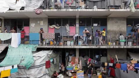 Reuters A school that is being used as a shelter, with people standing on balconies, washing hanging out and makeshift shelters made from tarpaulins, in Port-au-Prince, October 2025