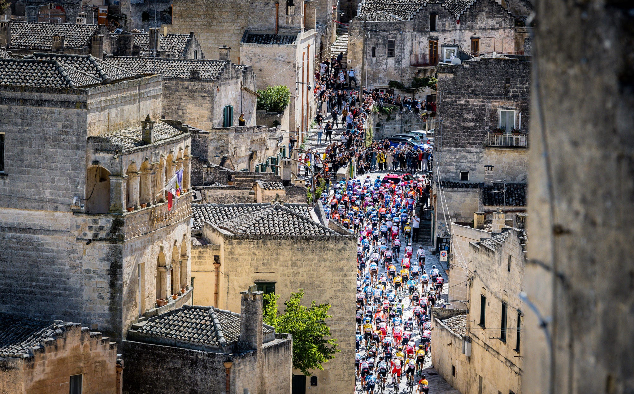rooftop view of large group of cyclists racing through an old city