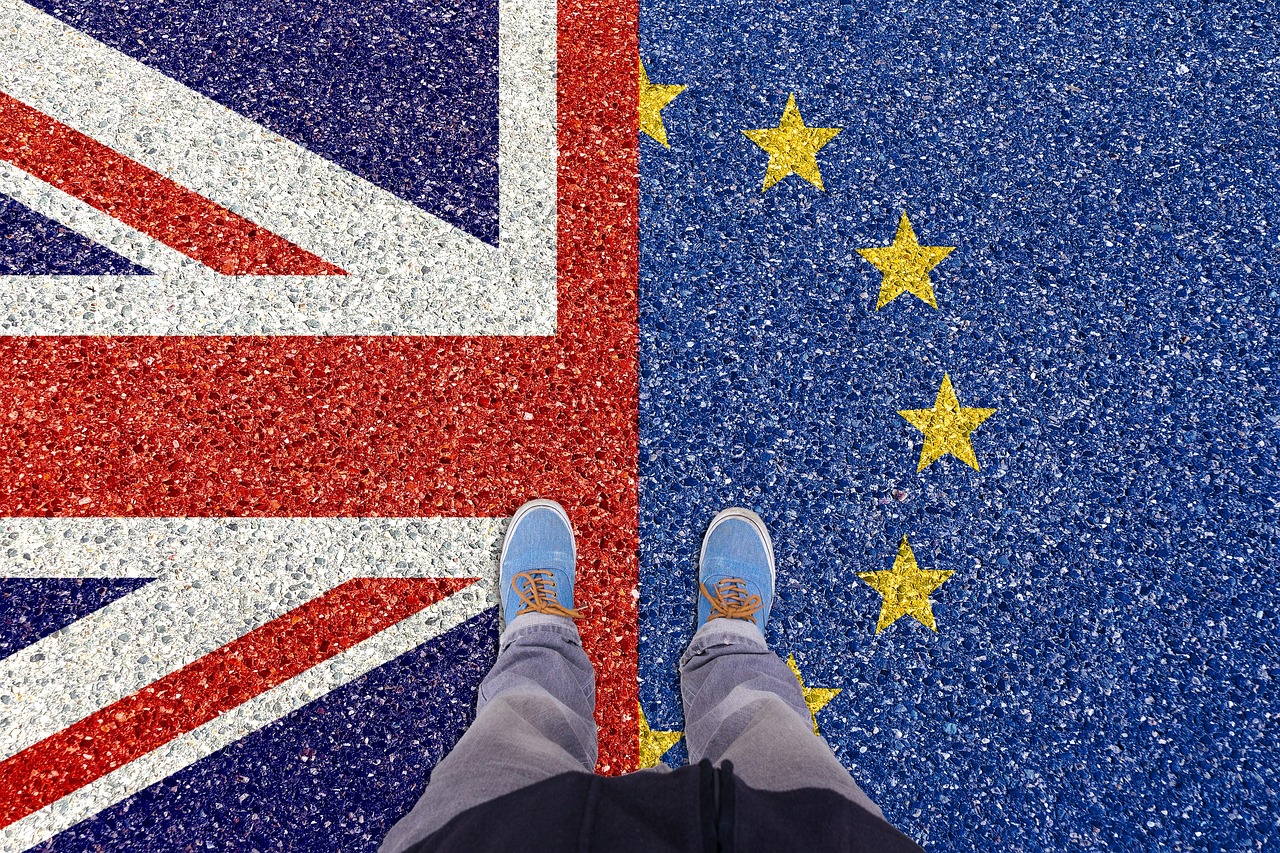 A person stands with one foot on the UK flag and the other on the EU flag painted on the ground.