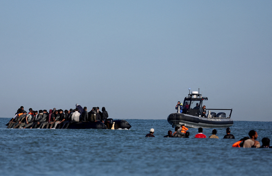 French gendarmes on a boat approach a group of migrants travelling on an inflatable dinghy leaving the coast of northern France in an attempt to cross the English Channel to reach Britain, from the beach of Petit-Fort-Philippe in Gravelines, near Calais, France, Aug. 25. [REUTERS/YONHAP]