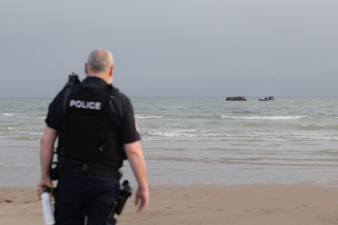 A police officer watches as a boat carrying migrants is approached by a French maritime gendarmerie vessel on the beach at Gravelines, France, July 2, 2025.