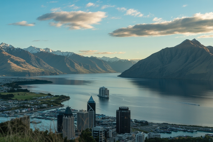 Scenic view of new zealand, with snow-capped mountains, a serene lake, and the city skyline, showcasing the natural beauty and vibrant atmosphere of the region