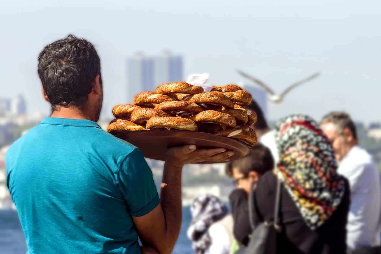 A street vendor carries a tray of traditional sesame-covered bagels known as simit along the Bosphorus waterfront in Istanbul, Türkiye. (Adobe Stock Photo)