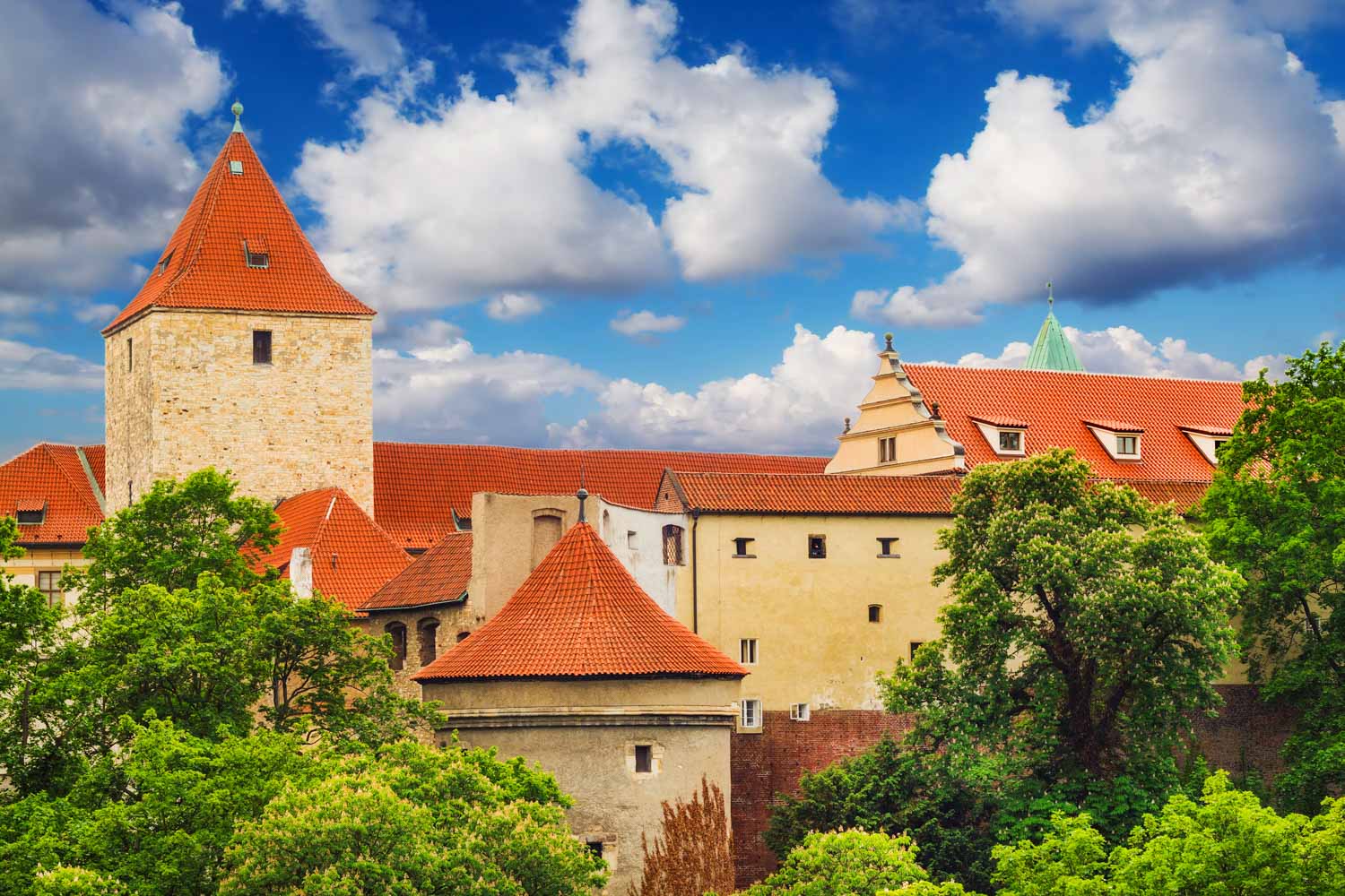 View of the Daliborka Tower and Lobkowicz Palace at Prague Castle on a sunny day, seen through the trees - one of the best places to visit in Prague with children