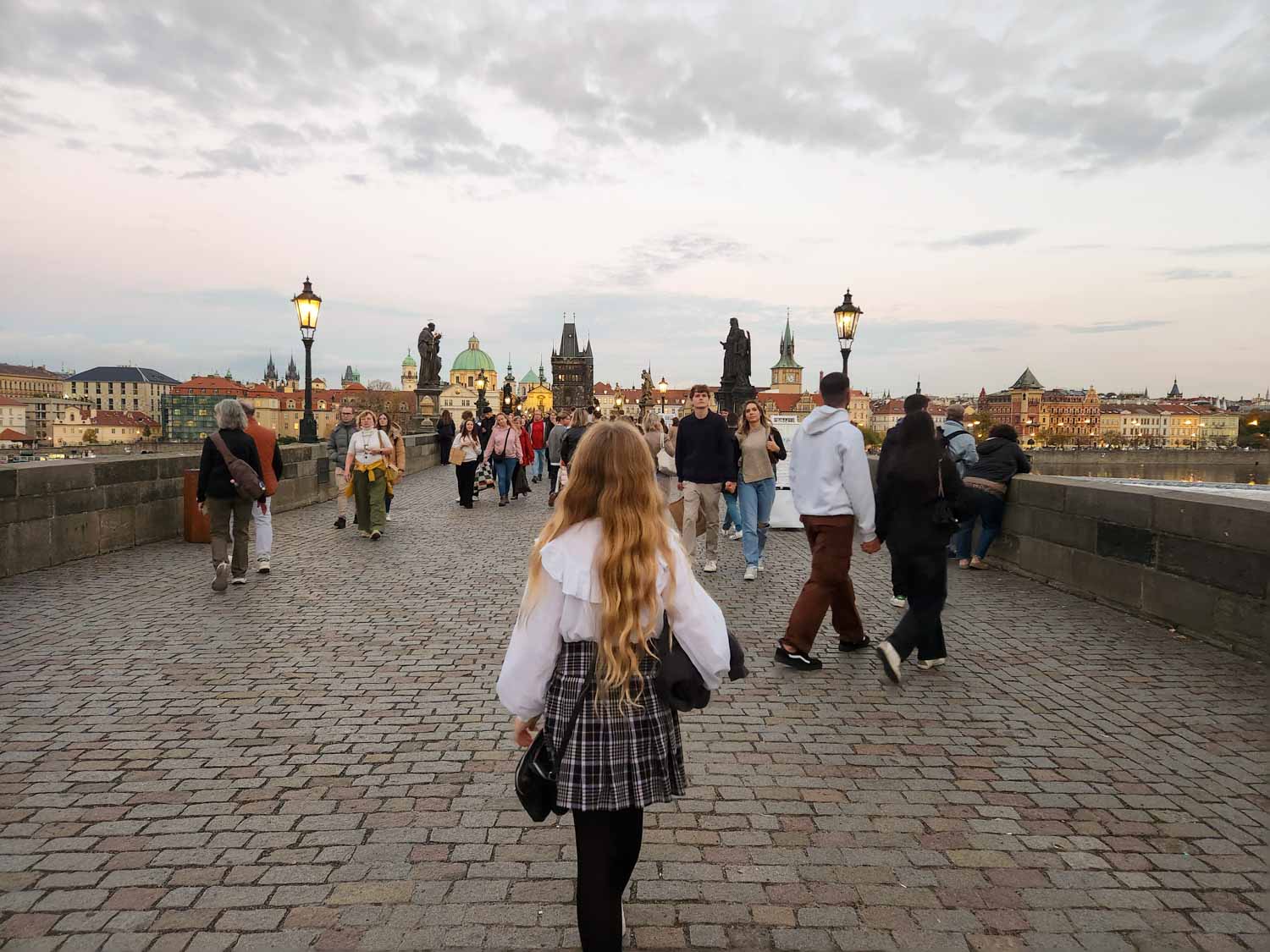 My daughter walks across the Charles Bridge just before sunset when there are fewer crowds with statues and buildings visible beyond