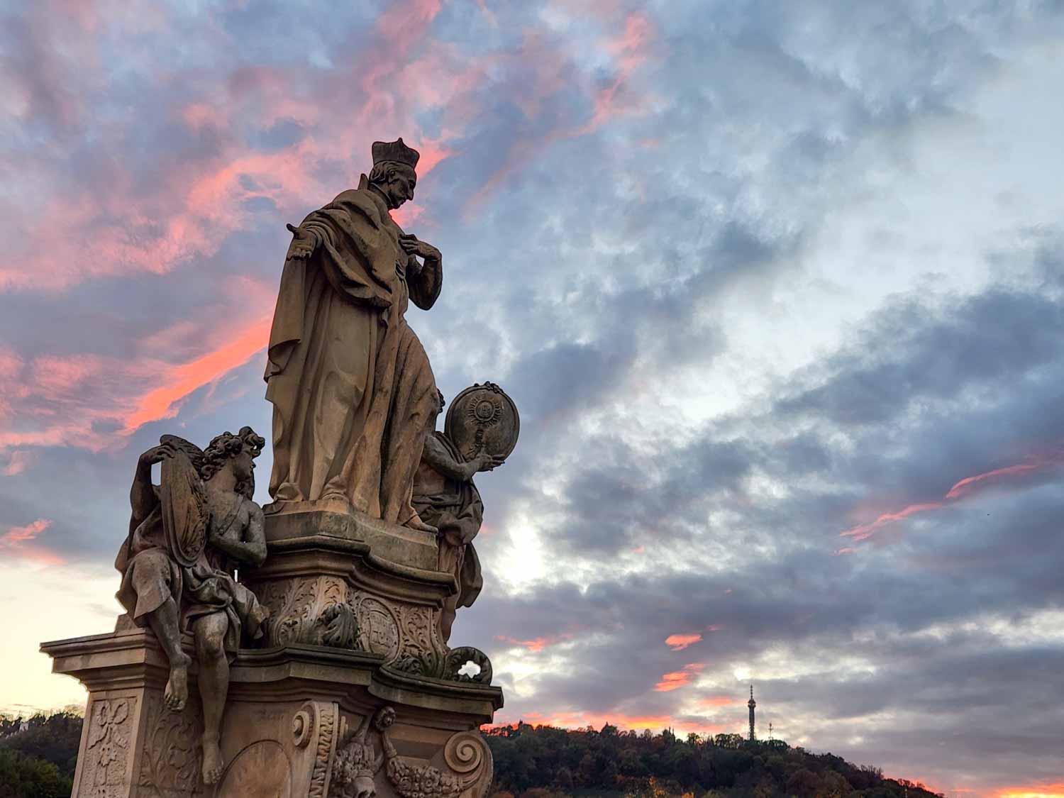 Statue of St Ivo on the Charles Bridge at sunset with red streaks in the sky behind - one of the unmissable sights in Prague with kids