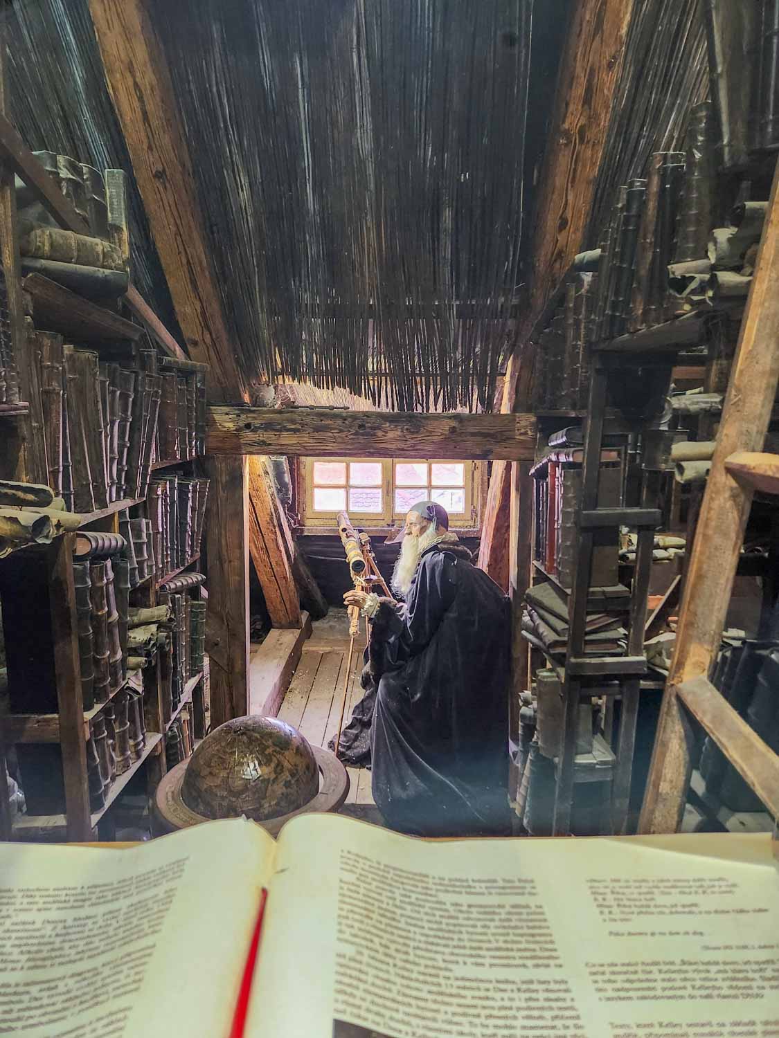 View across a book and globe to the figure of an old man with white beard at the Prague Museum of Alchemists and Magicians - one of the most unusual things to do in Prague with kids