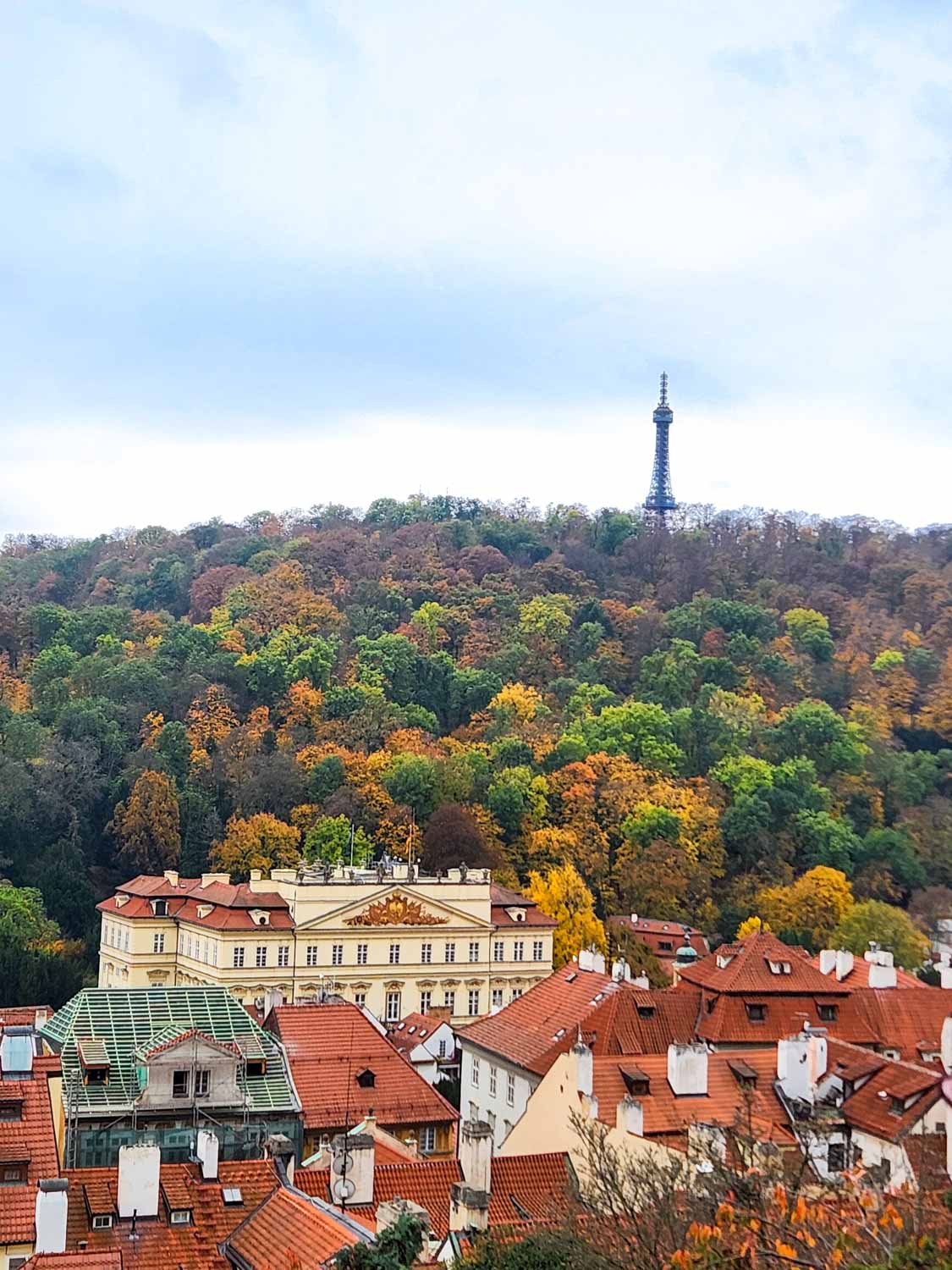 View towards Petrin Hill and its tower, with autumnal trees and the rooftops of the Mala Strana below - a visit is one of the fun things to do with kids in Prague