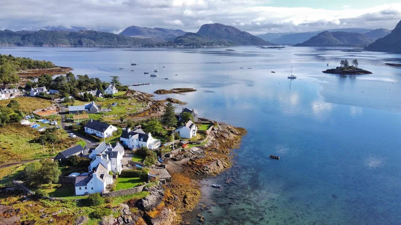 Charming white houses along the lakeshore of Plockton, with dramatic mountain peaks behind