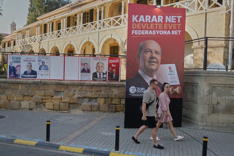 Two peopole walk past election signs on a city street.