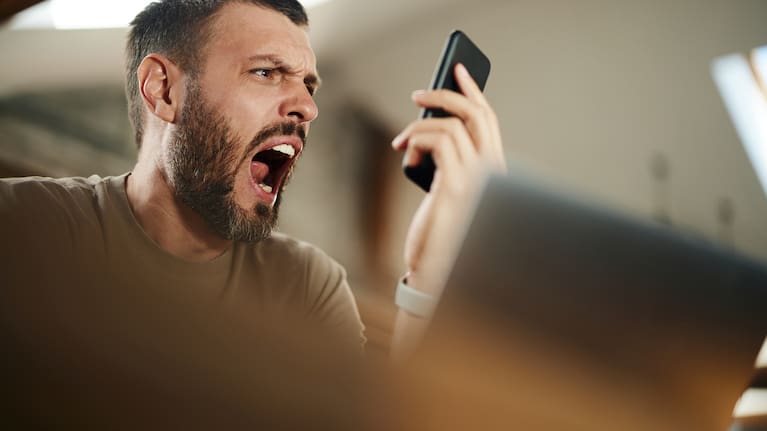 Frustrated man screaming on someone through a call over smart phone at home..