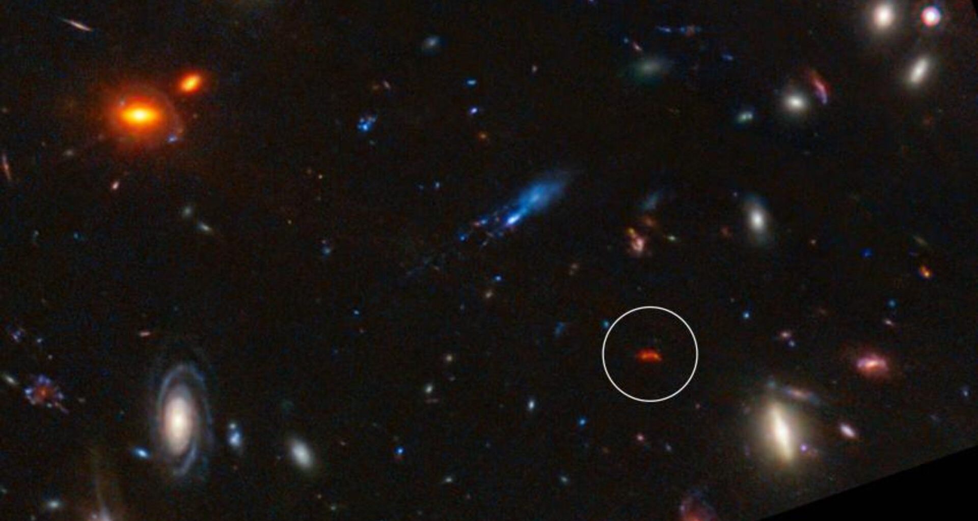 A deep space image showing the various colors of different galaxies, some red some white against a dark background