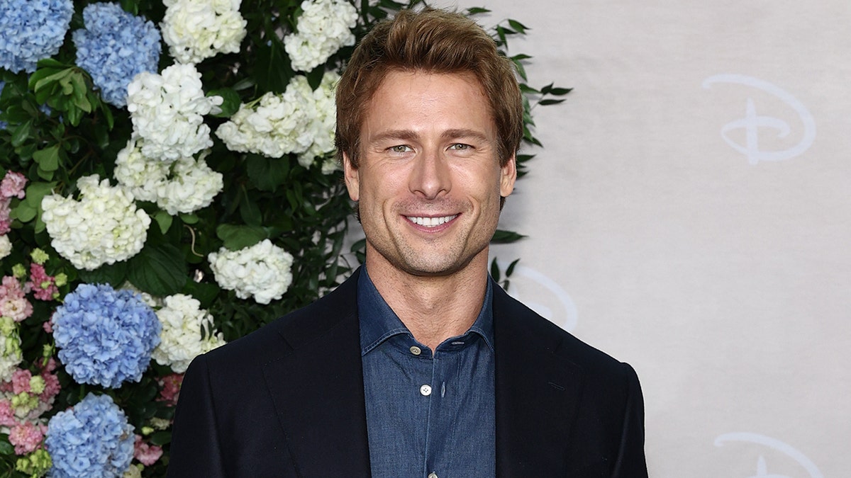 Glen powell in front of flowers.