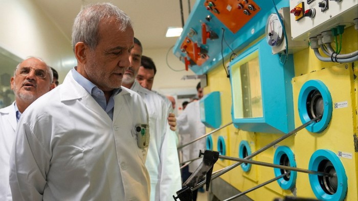 Iranian President Masoud Pezeshkian, wearing a lab coat, observes equipment during a visit to Iran’s nuclear facility in Tehran.
