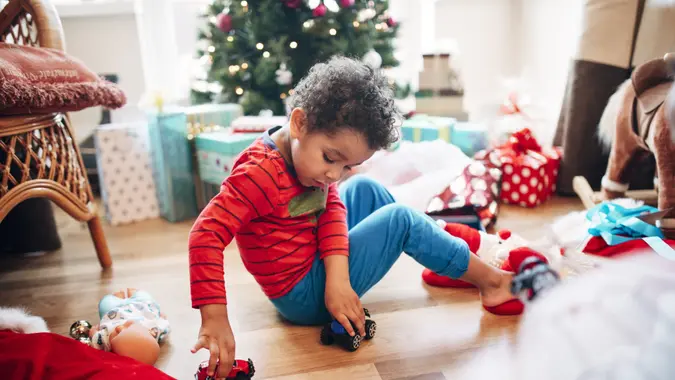 A little boy plays with some toy cars he has received as a Christmas present in front of the Christmas tree.