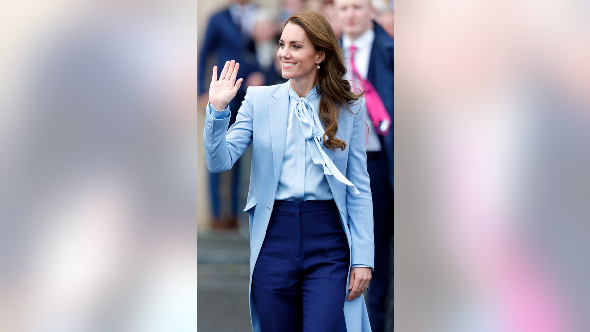 Kate Middleton wearing dark blue trousers with a matching light blue long coat and blouse.