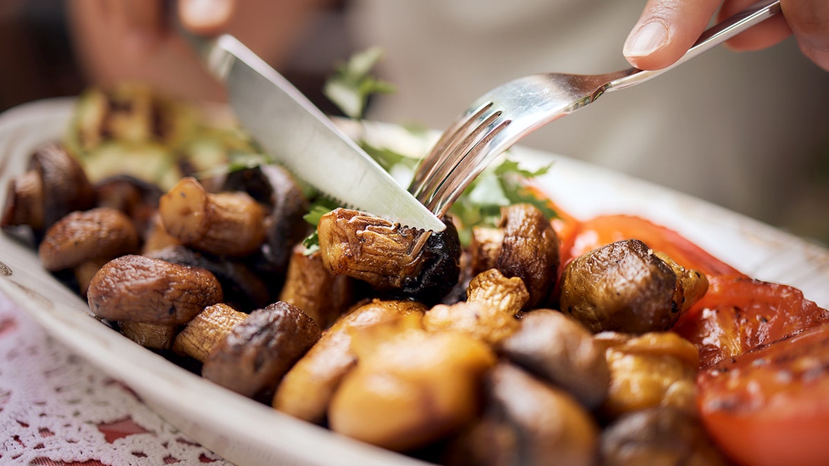 Close up of unrecognizable woman cutting roasted mushrooms during lunch in a restaurant.