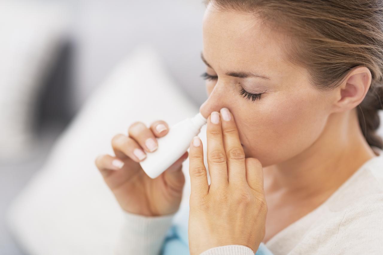 A woman demonstrates the use of nasal drops. (Adobe Stock Photo)