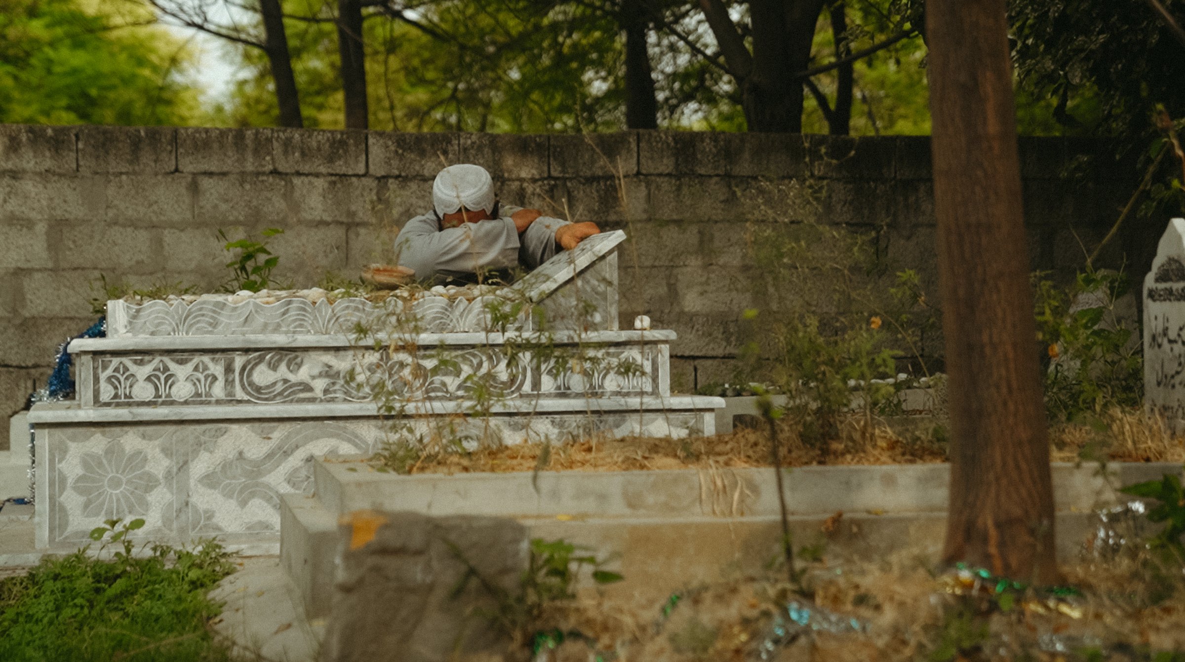 Un homme se penche sur une tombe dans un cimetière verdoyant.