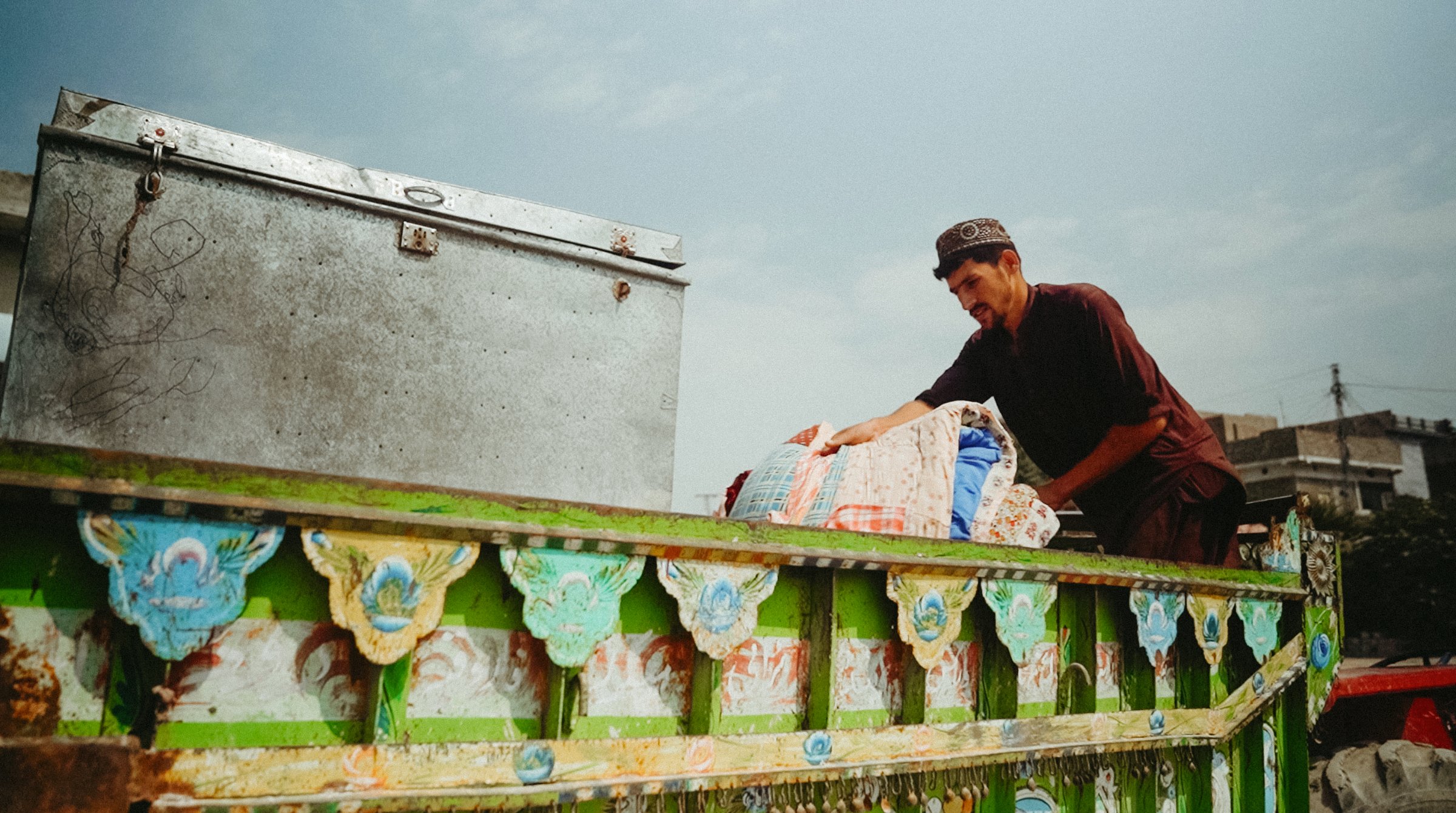 Un homme charge des sacs sur un véhicule coloré sous un ciel nuageux.