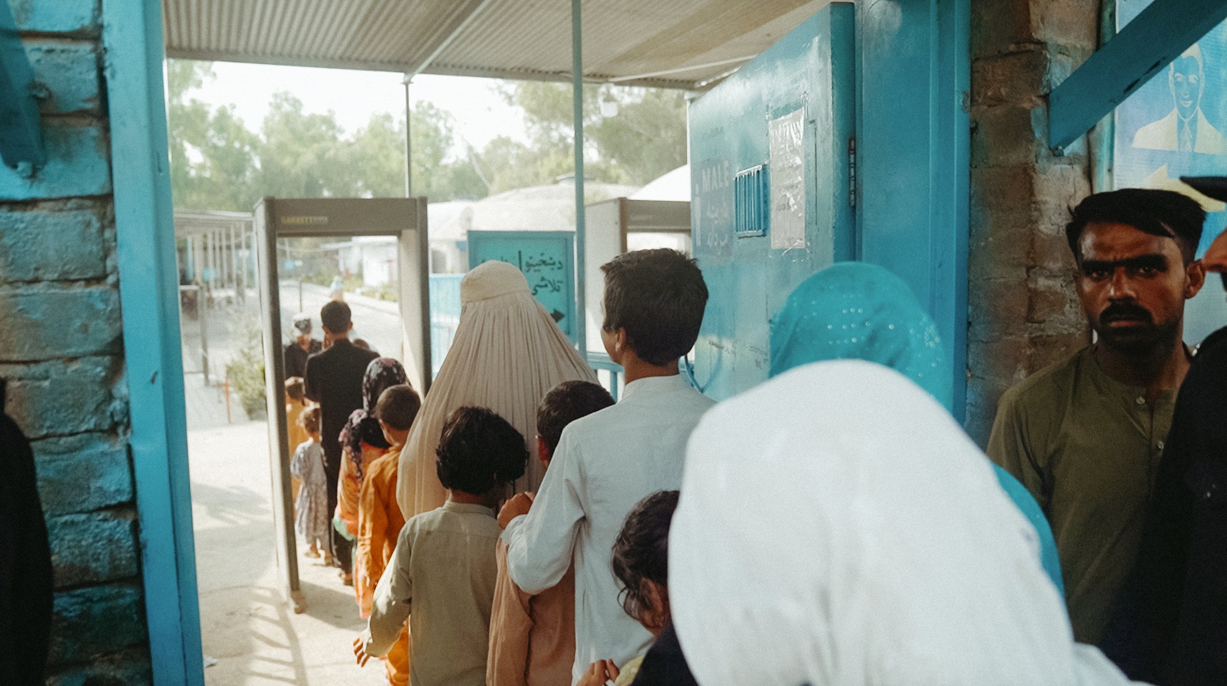 Une file d'attente de personnes, dont une femme en burqa, devant un bâtiment bleu.